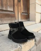 Botín de cuero negro con suela track, detalle de tira con hebilla lateral y costuras a la vista en el borde de la suela.