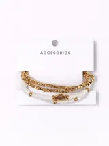 Pack de pulseras compuesto por dos unidades: una pulsera de cuentas metálicas doradas de forma cúbica y una pulsera de cuentas blancas con un dije central ovalado dorado y detalles metálicos.