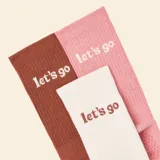 Pack de tres pares de medias de caña media con diseño acanalado y detalle de texto bordado. Incluye un par blanco, uno rosado y uno marrón, todos con suela antideslizante.