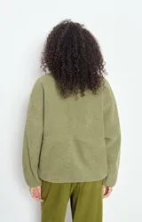 Campera de corderito con efecto shearling, color verde oliva, de corte holgado, cuello alto y cierre frontal completo. Presenta un pequeño parche con logo en el pecho.