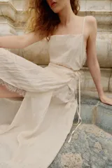 Vestido midi lencero de color blanco, confeccionado en tejido con efecto arrugado. Cuenta con escote recto, tirantes finos ajustables, diseño cruzado con cinturón fino para anudar y detalles de encaje en los acabados de la falda.