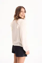 Blusa de viscosa color blanco con escote en V y cordón ajustable, mangas largas y volados decorativos en los hombros.
