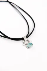 Gargantilla de cordón negro con dije plateado geométrico y piedra ovalada de tono celeste.