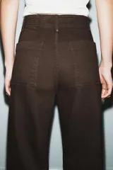 Jeans de tiro alto confeccionados en mezcla de algodón, con diseño de pierna ancha y costura marcada en el delantero. Presenta cintura con trabillas, cierre frontal con cremallera, botón y gancho metálico, y bolsillos de plastrón en la espalda.