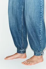 Jeans de tiro medio con diseño balloon, cinco bolsillos, cierre frontal con cremallera y botón metálico. Presenta un acabado en puño elástico en la parte inferior.