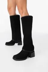 Bota de caña alta confeccionada en cuero gamuzado color marrón, con diseño de polaina desmontable que permite versatilidad en el estilo. Presenta una puntera redondeada y un taco cuadrado de altura media, ofreciendo un look clásico con un toque moderno.