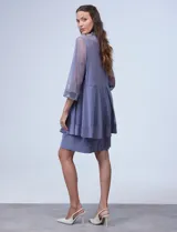 Conjunto de fiesta marca RM Richards, compuesto por vestido corto azul marino de seda fría con apliques bordados y chaqueta de seda fría con apliques bordados y mangas de microtul. El vestido tiene corte recto y largo a la rodilla. La chaqueta es abierta, con mangas 3/4 y largo a la cadera. El conjunto tiene forro interno a tono.