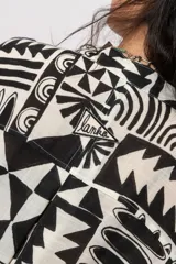 Camisa oversize de manga corta, con diseño estampado geométrico en blanco y negro, escote en V con cuello mao y cierre frontal con botones.