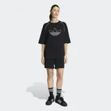 Remera Adidas de corte oversize, color negro, con cuello redondo y mangas cortas. Presenta el logo del Trifolio de la marca bordado en contorno blanco en el centro del pecho y detalles de líneas blancas en las costuras de las mangas.