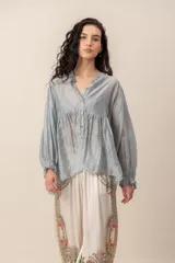 Blusa de seda gris con mangas largas abullonadas y puños con volados, escote en V con cuello fruncido y botones frontales.