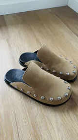 Zuecos color beige con tachas plateadas, base negra y plantilla con el logo de la marca.