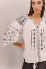 Blusa blanca con bordados en contraste de estilo bohemio, mangas amplias y diseño ligero.