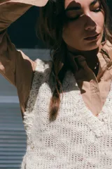 Chaleco tejido de lana rústica en color crudo, con cuello en V y aberturas laterales ajustables con lazos.