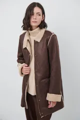 Chaquetón de efecto cuero en color marrón, con interior y detalles en corderito color bordó. Presenta cierre frontal con cremallera y botones a presión, cuello solapa y mangas largas con puños de corderito.