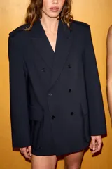 Blazer oversize de corte recto con cuello solapa y cierre frontal cruzado con botones. Presenta mangas largas con hombreras, trabillas en los hombros y grandes bolsillos de plastrón con solapa en el delantero. Incluye abertura en la espalda y forro interior.