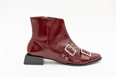 Bota corta de cuero charol color borgoña con punta fina y taco cuadrado negro. Presenta apliques de hebillas plateadas con ojalillos.