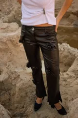 Pantalón de cuero negro con corte de jean y tiro medio, presenta apliques decorativos de rosetas en la parte delantera.