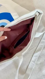 Tote bag de tela color blanco con estampado frontal de texto y corazón negro. Cuenta con cierre principal y bolsillo interno.