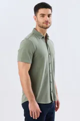 Camisa de piqué lisa color celeste, de manga corta, con cuello camisero y cierre frontal de botones oscuros.