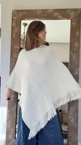 Poncho tejido en lana merino color marrón, con diseño de punto acanalado y terminación con flecos en el borde inferior. Incluye una pequeña etiqueta de cuero en la parte posterior.