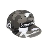 Gorro tipo snapback Supreme x New Era, con diseño de camuflaje en tonos grises y blancos. Presenta el logo Box Supreme en el frente y el logo de los New York Yankees bordado en blanco en el lateral.