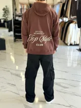 Canguro oversize de color marrón, con capucha y estampa en la espalda con el texto "Official Member of Top Style Club".