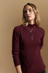 Polera de tejido acanalado color bordó, con cuello alto y diseño geométrico en relieve que estiliza la figura. Presenta un ajuste al cuerpo y mangas largas.