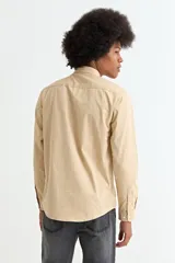 Camisa de manga larga en color beige, confeccionada en algodón, con cuello clásico y cierre frontal de botones.