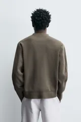Jersey de punto con textura, corte relajado, cuello redondo y manga larga con acabados en rib.