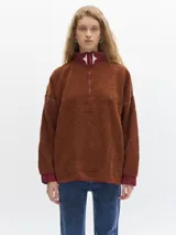 Buzo negro de fleece con cuello alto verde y cierre parcial con cremallera verde. Tiene puños con elástico azul y un bordado de un diamante blanco en el pecho.