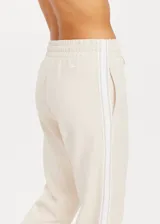 Pantalón deportivo color crema de corte recto con cintura elástica, cordón de ajuste y cinta de rayas plateadas en los laterales.