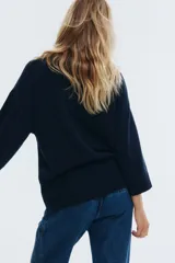 Buzo de punto fino en color azul marino, con cuello alto acanalado, mangas tres cuartos y hombros caídos. Presenta terminaciones acanaladas en puños y ruedo.