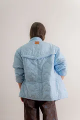 Campera reversible de estilo parka, color celeste, con diseño capitoneado con patrón de flores. Presenta ajuste elástico en la cintura, cuello alto y mangas largas. Incluye parche de marca en la parte superior de la espalda.