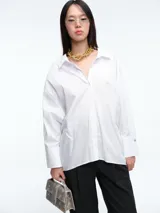 Camisa de corte recto y líneas clásicas, color blanco, con cuello camisero, cierre frontal de botones y puños anchos con botón.