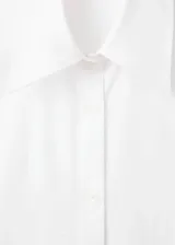 Camisa blanca de corte oversize y diseño largo, confeccionada en algodón. Presenta cuello camisero, cierre frontal con botones, mangas largas con puños abotonados y un distintivo diseño de espalda cruzada.