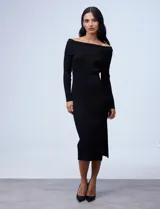 Vestido midi de punto rib, color negro, con escote bote y cuello volcado. Presenta mangas largas y un diseño ajustado al cuerpo con tajo lateral en el ruedo.