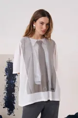 Remera blanca de manga corta con silueta amplia y cuello redondo. Presenta una estampa frontal que simula una camisa con corbata en tonos grises.