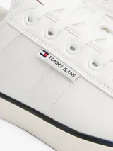 Zapatillas Tommy Jeans blancas de corte bajo con refuerzos de goma, suela vulcanizada con línea negra y logo en el lateral.