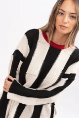 Buzo tipo poncho de corte oversize y holgado, con diseño de bloques verticales en colores blanco y negro. Presenta cuello redondo con detalle en color rojo, mangas largas y bolsillos laterales.