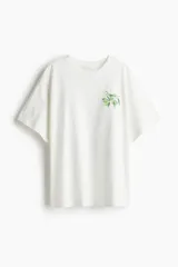 Remera de corte oversized confeccionada en punto de algodón, con cuello redondo acanalado, hombros caídos y bajo recto. Presenta un pequeño estampado de una rama de olivo en el pecho.