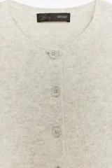 Chaqueta de lana 100% color gris claro, con cuello redondo, manga larga y cierre frontal con botones.