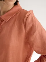 Camisa de lino color negro, con cuello clásico, cierre frontal de botones de madera y detalle de volados en los hombros. Presenta costuras a la vista en tono contrastante.