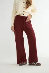 Pantalón de punto color crema, de corte recto y holgado, con cintura elástica y cordón ajustable. Presenta costuras verticales decorativas a lo largo de las piernas.