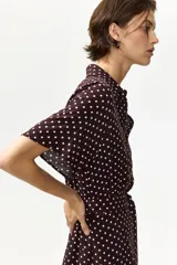 Vestido midi bordó con estampado de lunares blancos, cuello camisero, botonadura frontal y mangas cortas raglán. Cuenta con elástico en la parte posterior de la cintura y cinturón extraíble para atar.