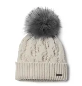 Gorro de lana tejido con diseño de trenzas, color beige, con borde acanalado y pompón de pelo sintético gris en la parte superior. Incluye una pequeña placa metálica con el logo de la marca en el borde.