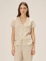 Camisa de lino y algodón color beige con patrón a cuadros, cuello en V y mangas cortas. Presenta un diseño de inspiración oriental con detalles de galones decorativos y botones frontales.