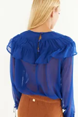 Blusa verde oliva con volados en el cuello y mangas largas transparentes con puños elásticos.