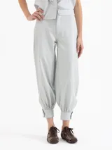 Pantalón de cuero ovino color gris claro, con frunces en el puño de la botamanga que aportan volumen. Tiene cintura doble con pespunte y botones forrados en cuero.
