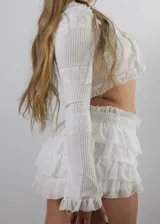 Conjunto de dos piezas compuesto por un top de manga larga con volados y cierre frontal con lazos, y una pollera corta con volados y cintura elástica.