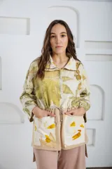 Buzo oversize color crema con estampado de hojas en tonos verde y amarillo, cuello alto con medio cierre metálico y jareta en la cintura para ajustar.